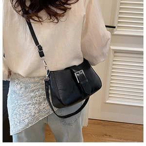 Detail of black textured leather crossbody bag with silver buckle worn by a model