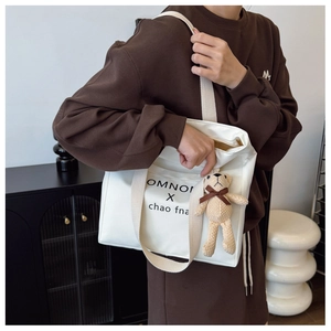 Detailed shot of white canvas tote bag with bear charm and chic minimalist print