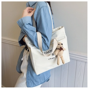 Close-up of minimalist white tote bag with black typography and cute bear plush charm
