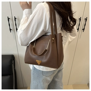 Detail of a brown leather tote bag with metal ring handle and triangular ornament