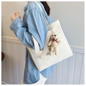 Detail of white canvas tote bag with black SURF X charm text and a knit bear pendant