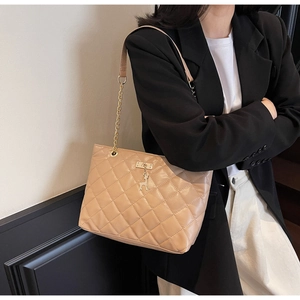 Detail of warm beige quilted tote bag with golden deer charm and chain shoulder strap