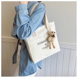 Detail of white nylon tote bag with teddy bear pendant and woven shoulder strap