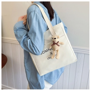 Detail of cream white tote bag with canvas strap and cute teddy bear charm accessory