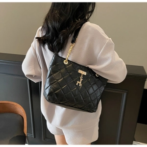 Detail of black quilted shoulder bag featuring gold chain strap and a deer charm