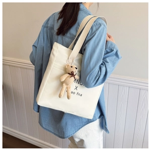 Chic beige canvas shoulder bag with a cute bear pendant shown on a model