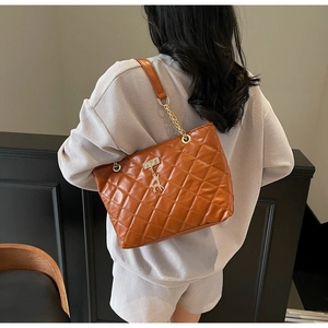 Rear view of a model wearing a brown quilted tote bag with golden deer charm
