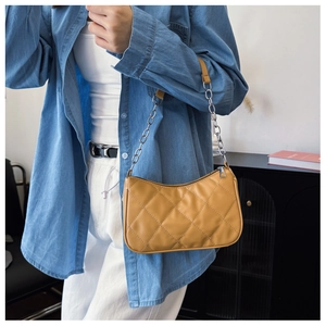 Detail der gelben Stepptasche mit silberner Kette, getragen über einem Jeanshemd
