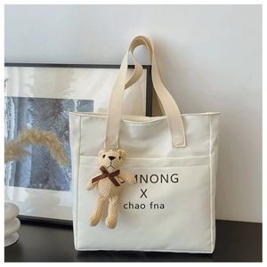 Detail of off-white canvas tote bag featuring black lettering and cute 3D knit bear charm