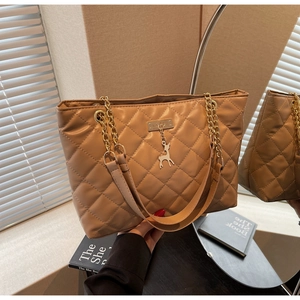 Quilted khaki tote bag featuring a gold chain strap and a deer charm on a vanity table
