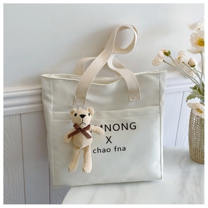 Close-up of cream square tote bag with black typography and cute yellow bear pendant