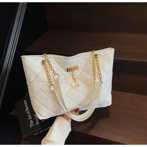 Detail of white quilted tote bag with gold deer charm and chain strap on stairs