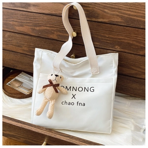 Detail of white canvas tote bag with black lettering and a cute beige bear charm accessory