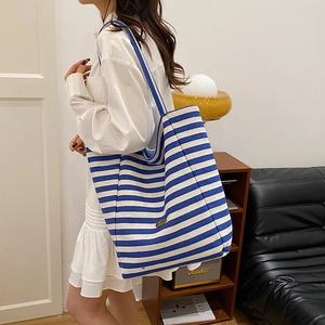Chic blue and white striped knit tote bag worn by a model in a minimalist urban setting