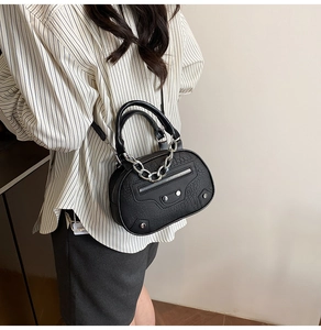 Detail of a chic black shell bag featuring textured leather and bold silver chain accents
