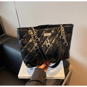 Detail of black quilted tote bag featuring silver deer pendant and chain shoulder strap