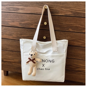 Close-up of white shoulder tote with black lettering and brown plush bear charm