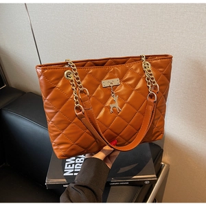 Detail of brown quilted tote bag featuring gold chain strap and a small deer charm