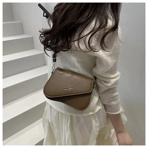 Détail d'un sac besace marron mat avec rabat incurvé et finitions métalliques argentées