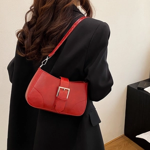 Red glossy leather shoulder bag with silver buckle worn over a black blazer jacket