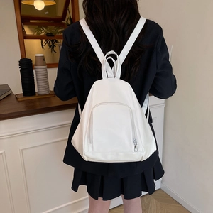 White minimalist triangular PU leather backpack for women shown in a casual cafe setting