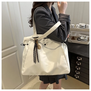 Detail of ivory tote bag with drawstring side and metal tennis racket charm on shoulder