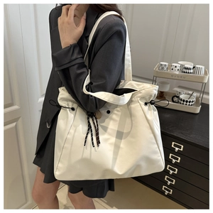 Detail of off-white tote bag with black drawstring and striped knot on a model shoulder