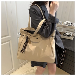 Detail of beige large capacity tote bag featuring drawstring closure and metal charm