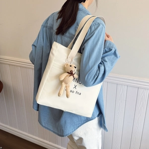 Minimalist white tote bag with black lettering and a brown plush bear charm accessory