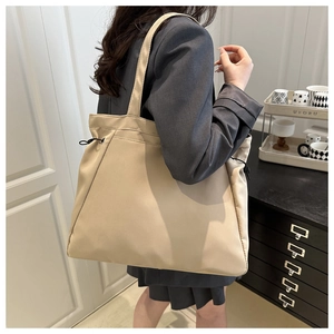 Detail of a large beige nylon tote bag with side drawstring shown on model for daily commute