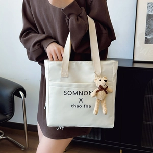 Minimalist off-white canvas tote bag with letter print and brown plush bear charm