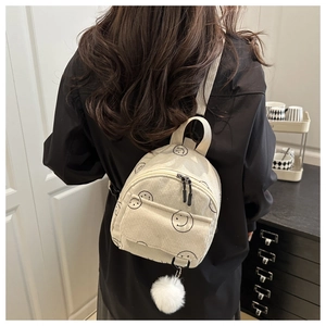 Close-up of beige corduroy mini backpack with black smiley face patterns and plush pom-pom