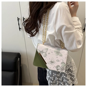 Détail du sac bandoulière à motif papillon avec chaîne dorée porté par le mannequin