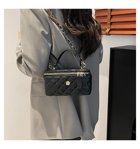 Detailed back view of model wearing black quilted box bag with gold chain and flower logo