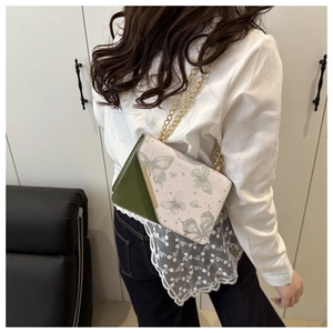 Détail du sac bandoulière en cuir vert avec motif papillon et chaîne dorée chic