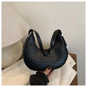 Detailed view of black textured crescent bag on a wooden table with soft lighting