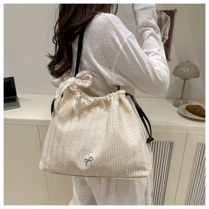 Detail of off-white woven tote bag featuring a black drawstring and lace floral bow decoration