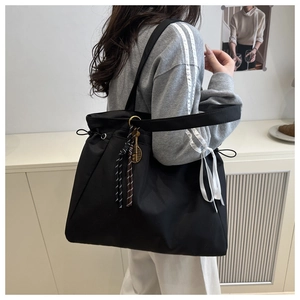Detail of black nylon tote bag featuring adjustable drawstring and white ribbon decoration