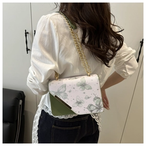 Détail d'un sac blanc à motif papillon avec bandoulière en chaîne dorée porté