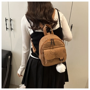 Detailed view of brown corduroy backpack with smiley face print and white pompom charm