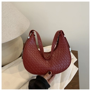 Detail of burgundy woven leather texture and silver hardware on crescent shoulder bag