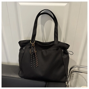 Detail of black large capacity tote bag with side drawstring and woven rope charm pendant