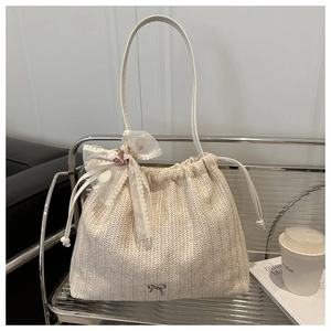 Detail of cream woven tote bag featuring delicate lace bow and silver butterfly charm