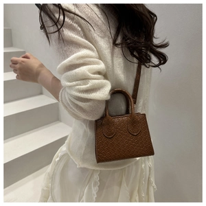 Detail of a dark brown mini woven patterned handbag worn with an elegant white lace outfit