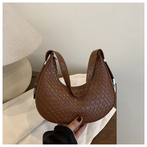 Macro detail of brown woven crescent bag with leather strap and metal buckle