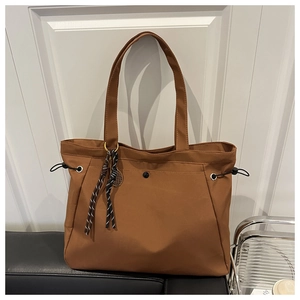 Close-up of brown tote bag featuring front snap pocket and stylish black drawstring details