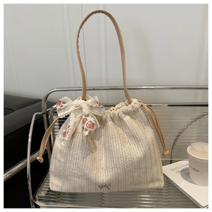 Detail of beige woven tote bag with lace floral embroidery and leather handles on a shelf