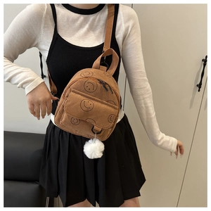 Detail view of brown corduroy backpack with smiley face pattern and white fuzzy ball charm