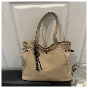 Detail of beige nylon tote bag featuring drawstring side and woven knot charm accent