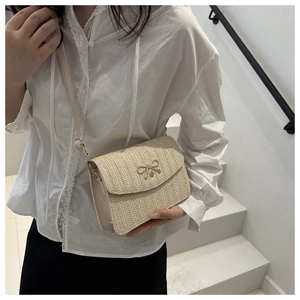 Detail of woven crossbody square bag with gold bow clasp on elegant model in stairway